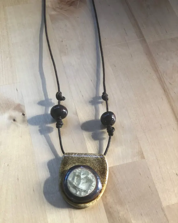 Collana Luna — Ciondolo bronzo con un disco perlato, su cordino con perline nere.