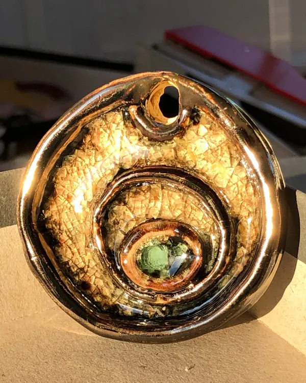 Ciondolo Spirale d'Oro — Smalto bronzo e oro avvolto a spirale attorno a una goccia di vetro verde.
