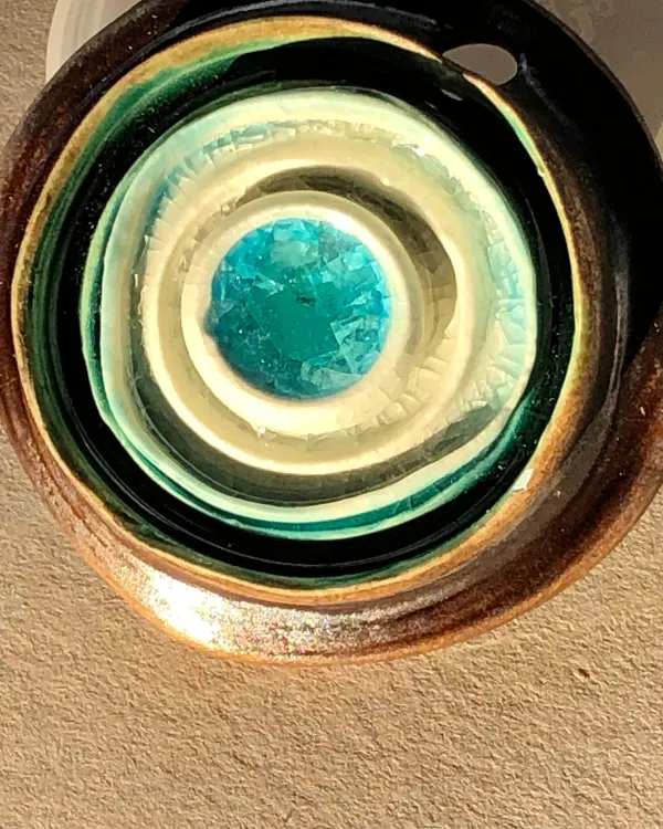 Ciondolo Vortice — Cerchi concentrici color crema e bruno attorno a un cuore di vetro turchese.